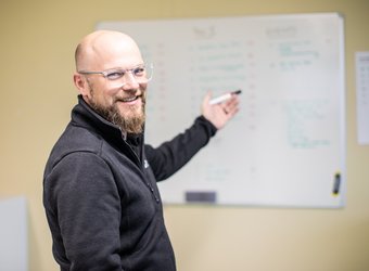 Der Projektverantwortliche Marco Gurtner lacht in die Kamera, während er auf eine Leinwand deutet.